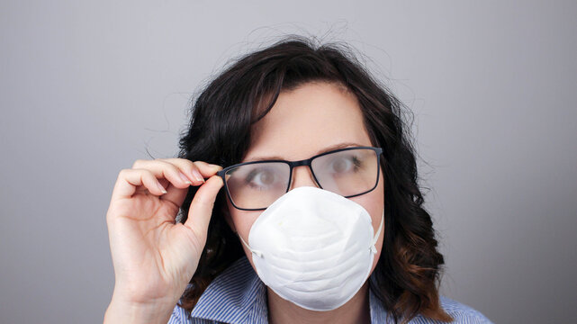 Young woman with foggy glasses caused by wearing disposable mask on white background. Protective measure during coronavirus pandemic