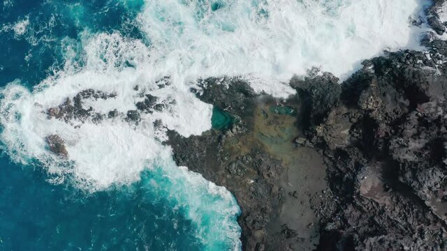 People swimming in beautiful blue pools on summer day. Top down view of tourists enjoying water in natural volcanic tide pools at stormy Pacific ocean on tropical Maui Hawaiian island, USA aerial 4K