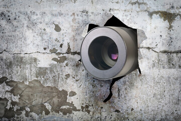 Concept of paparazzi or hidden camera, camera lens looks out through a hole in broken grunge wall