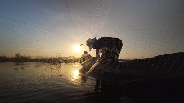 Footage B roll of Silhouette fisherman throwing fishing net during sunset with boats at the lake. Traditional culture of Thailand. Concept Fisherman's life style.