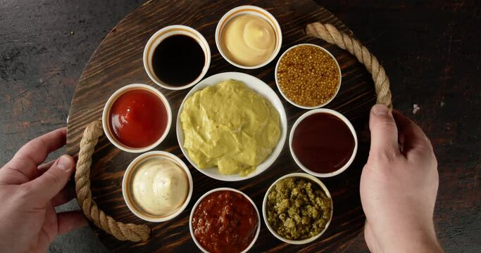 Men's hands are put on table with different types of sauces. 