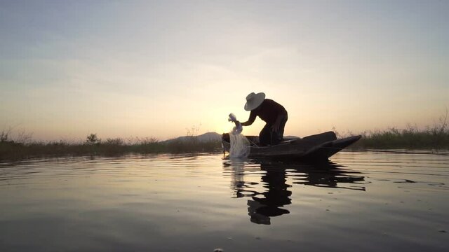 Footage B roll of Silhouette fisherman throwing fishing net during sunset with boats at the lake. Traditional culture of Thailand. Concept Fisherman's life style.