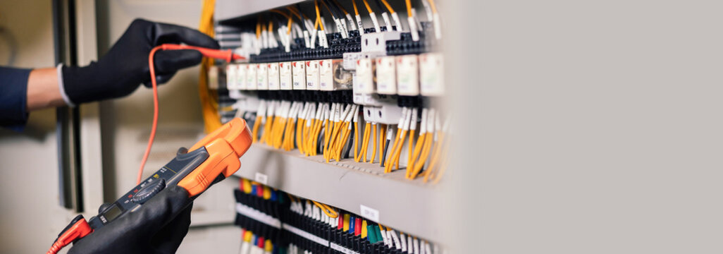 Electrician engineer work tester measuring voltage and current of power electric line in electical cabinet control.and wires on relay protection system. Bay control unit. Medium voltage switchgear.