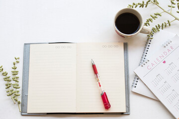 notebook planner ,calendar for business work with hot coffee arrangement flat lay style on table white at office desk