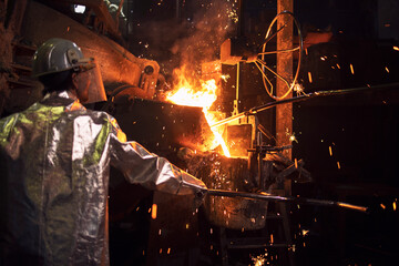 Smelting of metal in large foundry. Iron and steel being melted in furnace. Worker controlling...