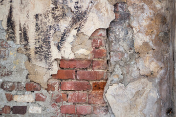 The texture of the old wall. The plaster fell off. Brickwork collapses over time. Dangerous section of an old building. Red brick sticks out from under the plaster layer.