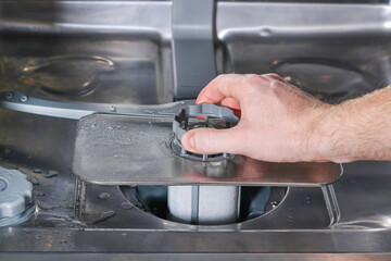 Man unscrews the filter for cleaning in the dishwasher.