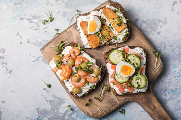 Variety of sandwiches for breakfast, snack, appetizers - tempeh, salmon, prawns grilled whole grain bread sandwiches with microgreens on a light background