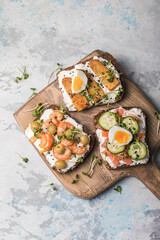 Variety of sandwiches for breakfast, snack, appetizers - tempeh, salmon, prawns grilled whole grain bread sandwiches with microgreens on a light background