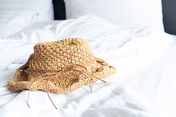 A wicker hat placed on a white bed in a bright bedroom. Get ready to travel