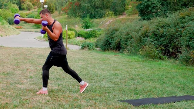 Boxer man training workout with dumbbell outdoor. Fighter defence fight punch exercise. Man in black training strong combat punch with dumbbells in park