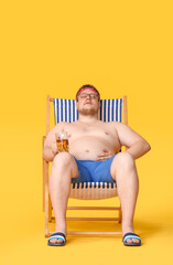 Overweight man with glass of beer sitting on beach chair against color background. Weight loss...