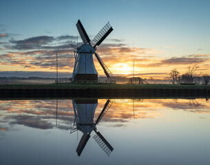 A tranquil winters dawn at a windmill reflected in a canal.