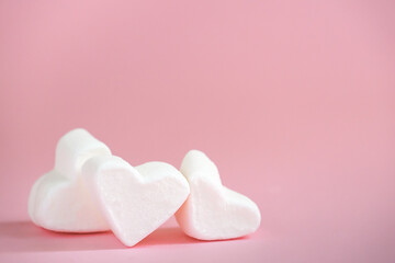 Fototapeta premium Three white marshmallows in the shape of a heart on a pink background