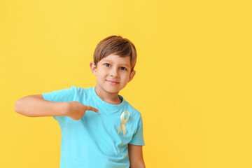 Little boy with golden ribbon on color background. Childhood cancer awareness concept