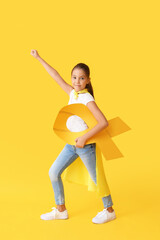 Little girl with golden ribbon wearing superhero costume on color background. Childhood cancer awareness concept