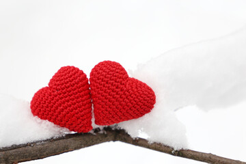 Fototapeta premium Valentine hearts in winter forest, cold weather. Two red knitted hearts on snow covered branch, symbol of romantic love, background for holiday