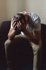 A young man in a state of crisis and despair. The white guy is sitting on a chair and holding his...