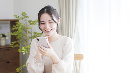 リビングでスマートフォンを見る若い女性