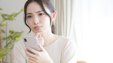 リビングでスマートフォンを見る若い女性