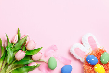 Happy easter. Multi-colored eggs in the nest, rabbit ears, flowers on a pink background. Flat lay greeting card.