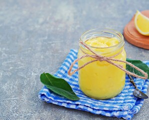 Lemon curd, a sweet fruity custard in a glass jar on a gray concrete background. Cream recipes.