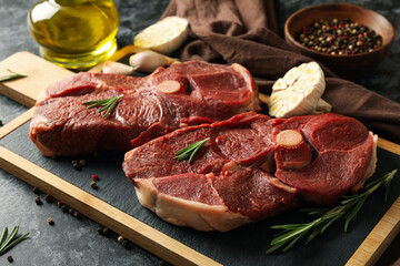 Board with raw steak meat, herbs and spices on black smokey background