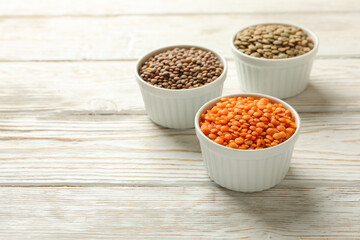 Bowls with different legumes on wooden background, space for text