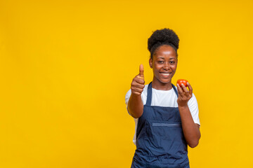 portrait of a smiling african chef holding a tomato and giving a thumbs up