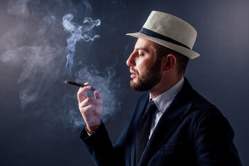 Portrait of an attractive business man with a cigar in black background studio