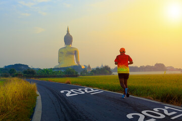 Obraz premium New year 2022 or start straight concept. word 2022 written on the asphalt road With male runner That runs among nature and the Big Buddha in Thailand That's like stepping into 2022.
