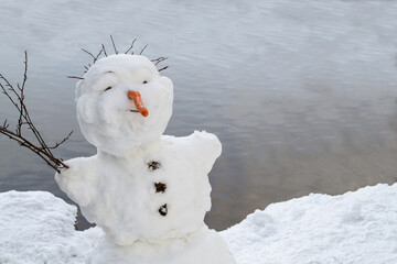 A cheerful, smiling snowman stands on the shore of the lake.