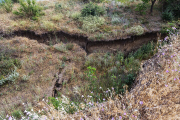 Mountain landslide disaster in sesmically dangerous area. Large cracks in earth, descent of large layers of earth blocking road. Mortal danger of damming people at foot of landslide slopes of mountain