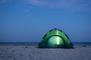 Tent is lit up at night. Camping by the seashore. Active tourism