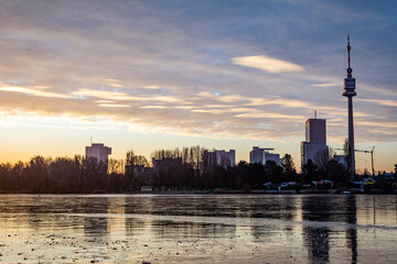 Fototapeta premium Beautiful morning scene at the so-called old Danube River in Vienna, Austria. View of a cold winter morning with a frozen lake and sun just above the horizon. Tranquil winter scene. 