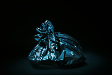 Plastic pollution. Waste collection. Ecology problem. Nature conservation. Black polyethylene garbage bag full with trash isolated on dark empty space background.