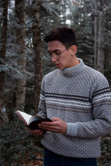 A young guy is reading a book in the forest. Winter landscape. Human and nature.