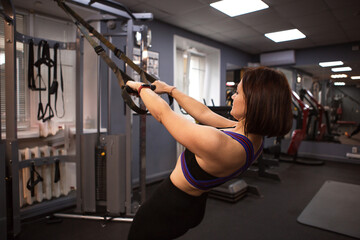 Woman in sportswear works out in the gym on a simulator for the strength of her back and arms. Sports form, healthy lifestyle, pumping iron, weight lifting. Muscle building, weight loss