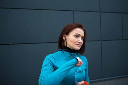 Woman in sportswear drinking clean water from a bottle during a workout on the street. Running, fitness, active healthy lifestyle, outdoor sports, water balance
