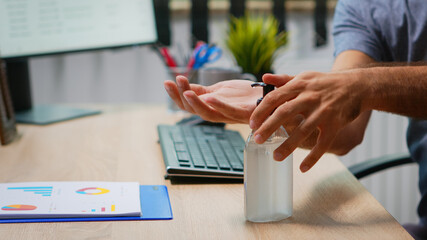 Close up of man using antibacterian gel before writing on computer. Entrepreneur working in new...