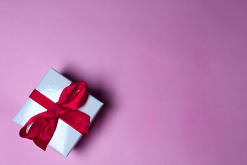 WHITE GIFT WITH RED RIBBON ON PINK BACKGROUND