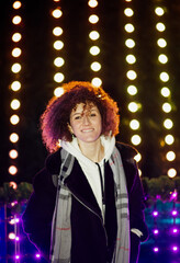 Young woman with curly hair against the background of glowing Christmas lights. Vertical portrait