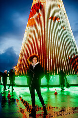 Portrait of young woman against the background of a city Christmas tree decorated with lights.