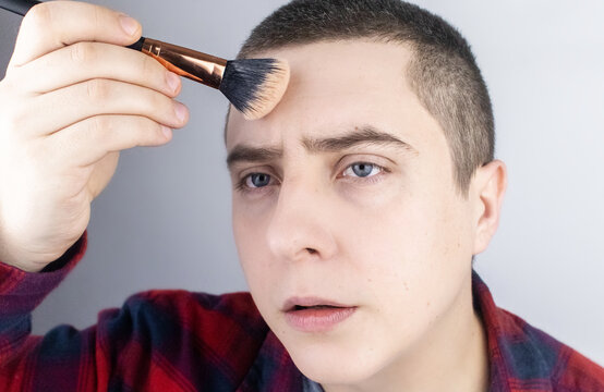 The Man Looks Into The Frame And Uses Powder. Close-up Of A Guy Putting Makeup On His Face. LGBT Community, Gay Or Self-care Concept.