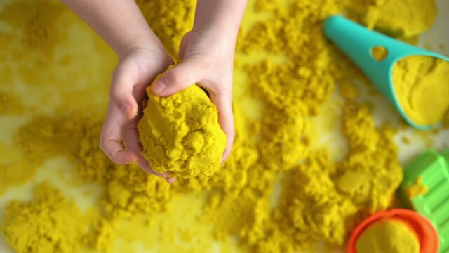 Close up of kids hands playing with yellow magic sand, top view. Development of fine motor skills, early education, sensorics.