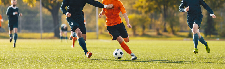 Horizontal image of football players running in a duel on a tournament match. Soccer forward player compete with defender. Anonymous football players kicking league game - obrazy, fototapety, plakaty