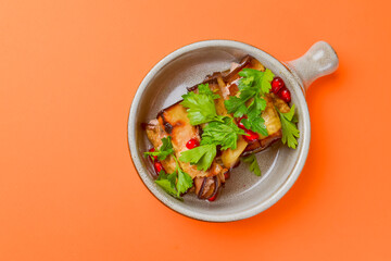Egg-plant rolls with meat and pomegranate seeds served in a bowl over orange background.