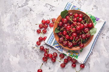 Bowl with red cherry on gray background, top view