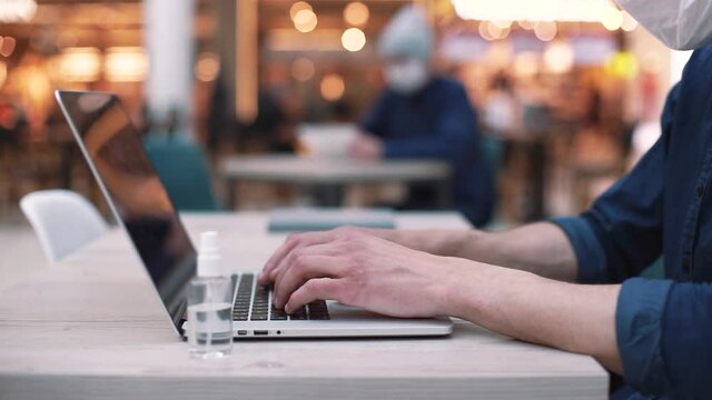 man in a face mask works on a laptop in a night cafe. close - up .