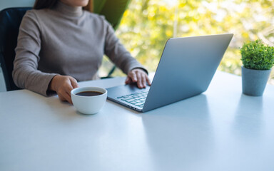 Fototapeta premium Closeup image of a woman working and touching on laptop computer touchpad while drinking coffee